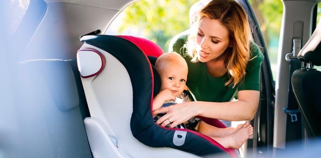 Mutter befestigt Kindersitz im Auto
